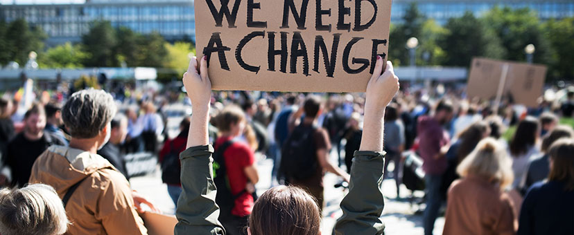 Woman at protest holds sign that reads “We Need Change” Woman at protest holds sign that reads “We Need Change”