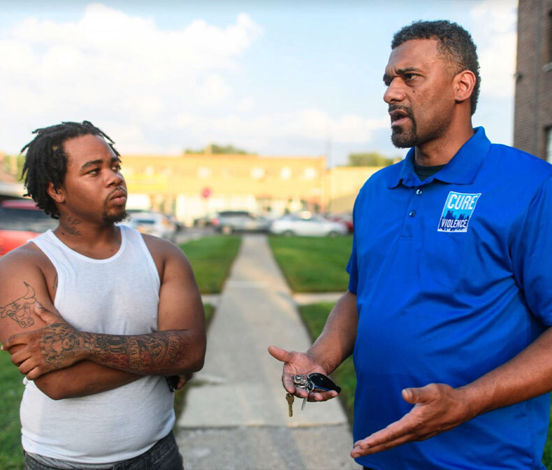 Two men speaking one is wearing a Cure Violence shirt